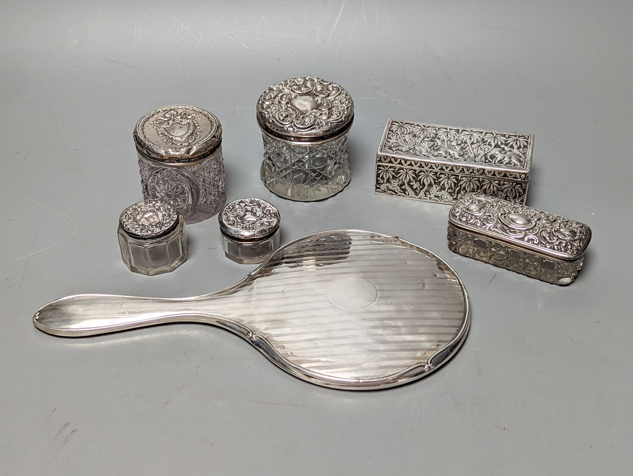 A silver mounted hand mirror, five assorted silver mounted glass toilet jars and an Indian white metal rectangular box.